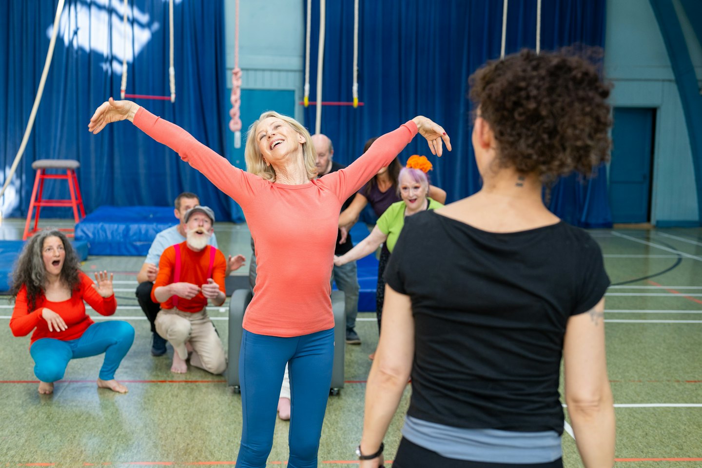 Un gruppo eterogeneo di adulti si diverte in una vivace lezione di fitness al chiuso.